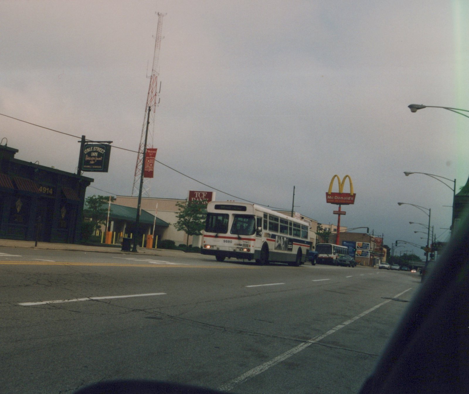 A white and red CTA bus drives down a city street on an overcast day, with a McDonald's sign and a TCF Bank sign visible in the background.