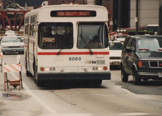 Front view of a white CTA bus with a red stripe, number 9868, displaying route 125 Water Tower Express, surrounded by city traffic on a cloudy day.