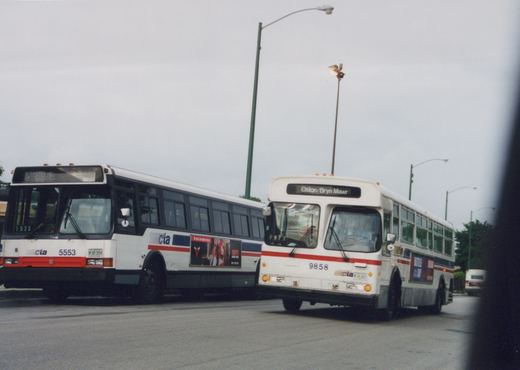 Two white CTA buses, one numbered 5553 and the other 9858, are on a street under an overcast sky; the bus on the right displays 'Elston/Bryn Mawr' as its destination.