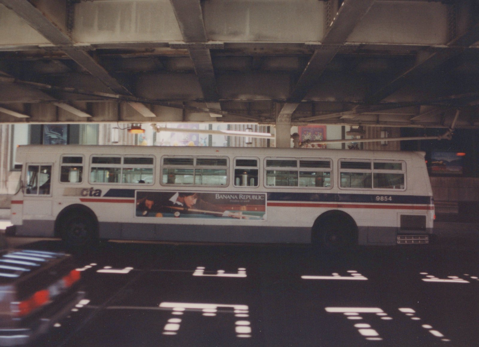 Side view of a white Chicago Transit Authority trolleybus with '9854' on its rear, under a bridge, featuring a Banana Republic ad.