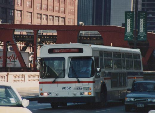 A white CTA bus with a red stripe, number 9852, is on a city street with its destination sign reading '125 Water Tower Express Railroad Stations'. An elevated structure and a green banner for 'Chicago Collective' are in the background.