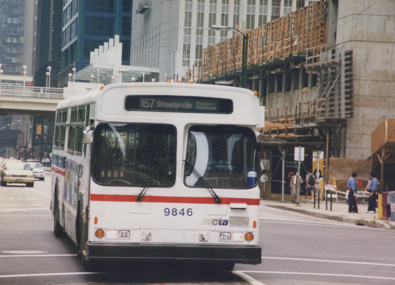 A white and red Chicago Transit Authority bus with the number 9846 is driving down a city street with tall buildings and construction in the background.