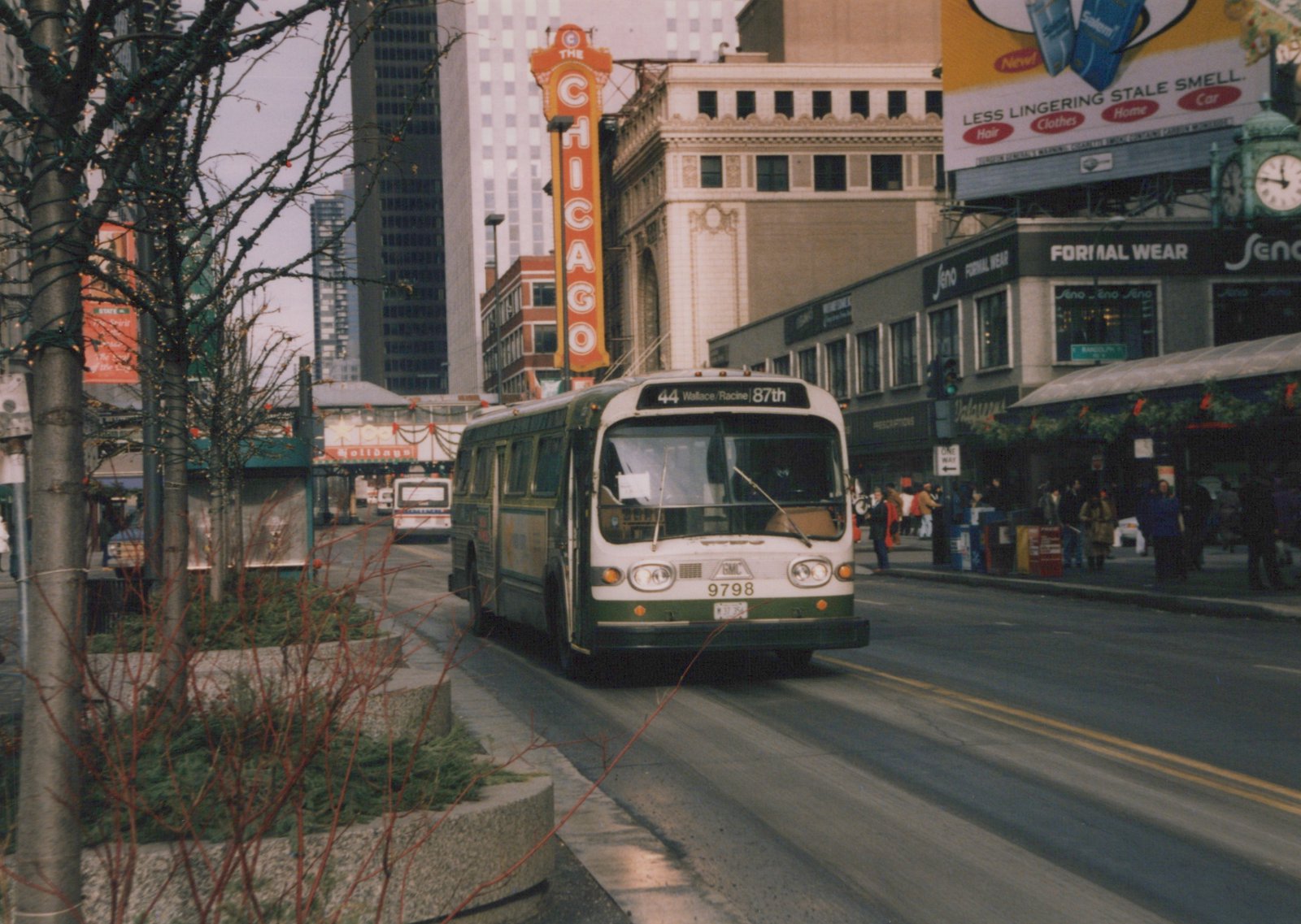 A green and white city bus drives down a street in winter, with bare trees, holiday lights, and the Chicago Theatre sign visible in the background.