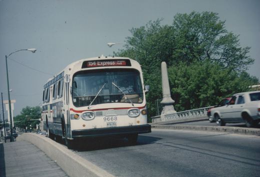 A white and red Chicago Transit Authority bus with the number 9668 and destination sign reading 154 Express Wrigley Field is shown crossing a bridge on a sunny day, with trees and another car visible in the background.