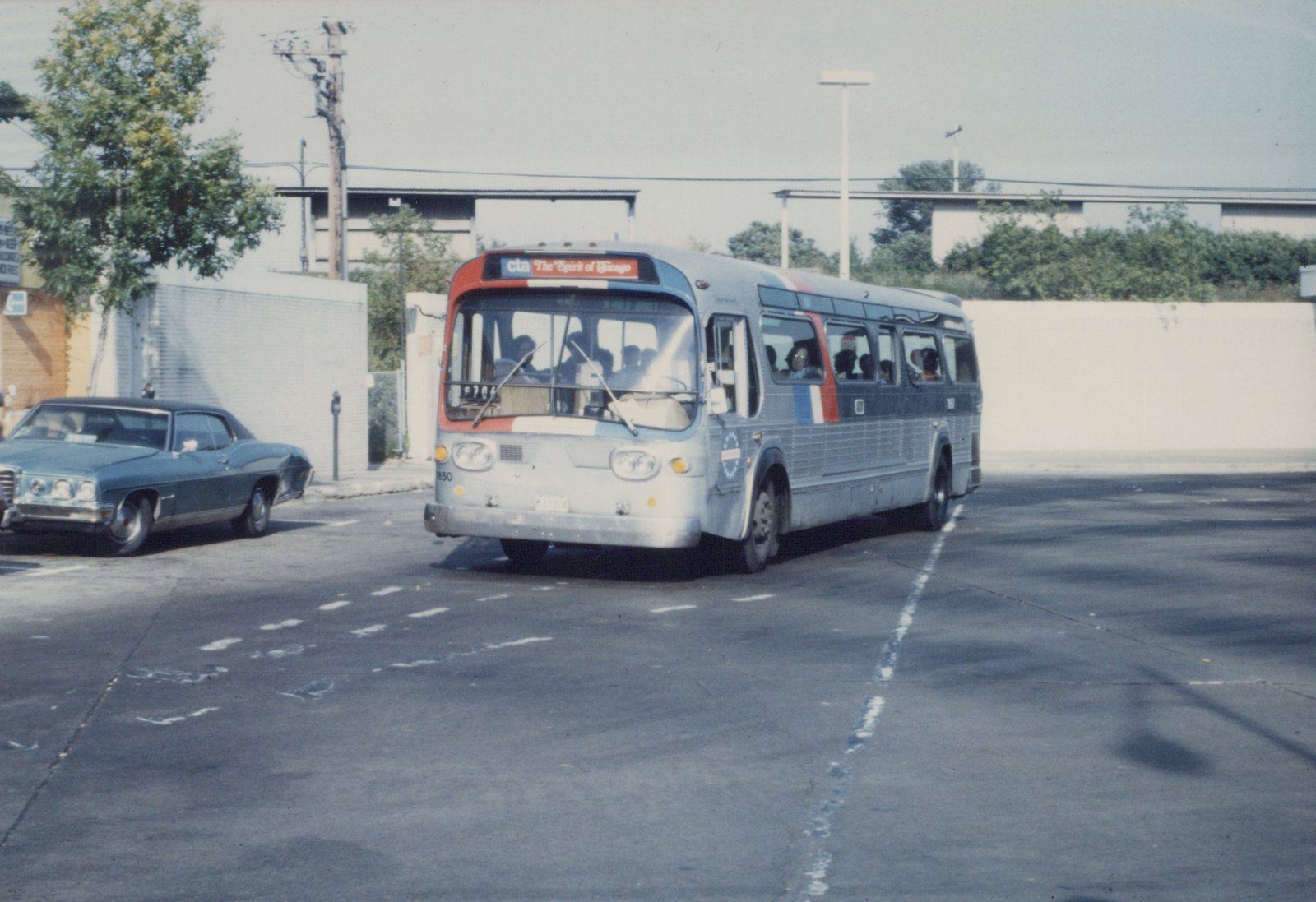 A vintage CTA bus with the number 750 and 'The Spirit of Chicago' on its sign is driving down a street, with a blue car parked nearby.