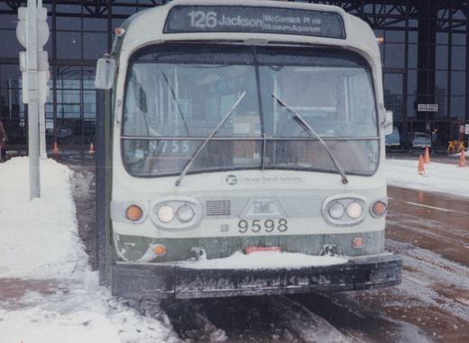 Front view of a white and green CTA bus with the number 9598 and destination sign reading 126 Jackson McCormick PI via Museum Aquarium, parked on a snowy street in front of a large building with a sign for the Auto Show Entrance.