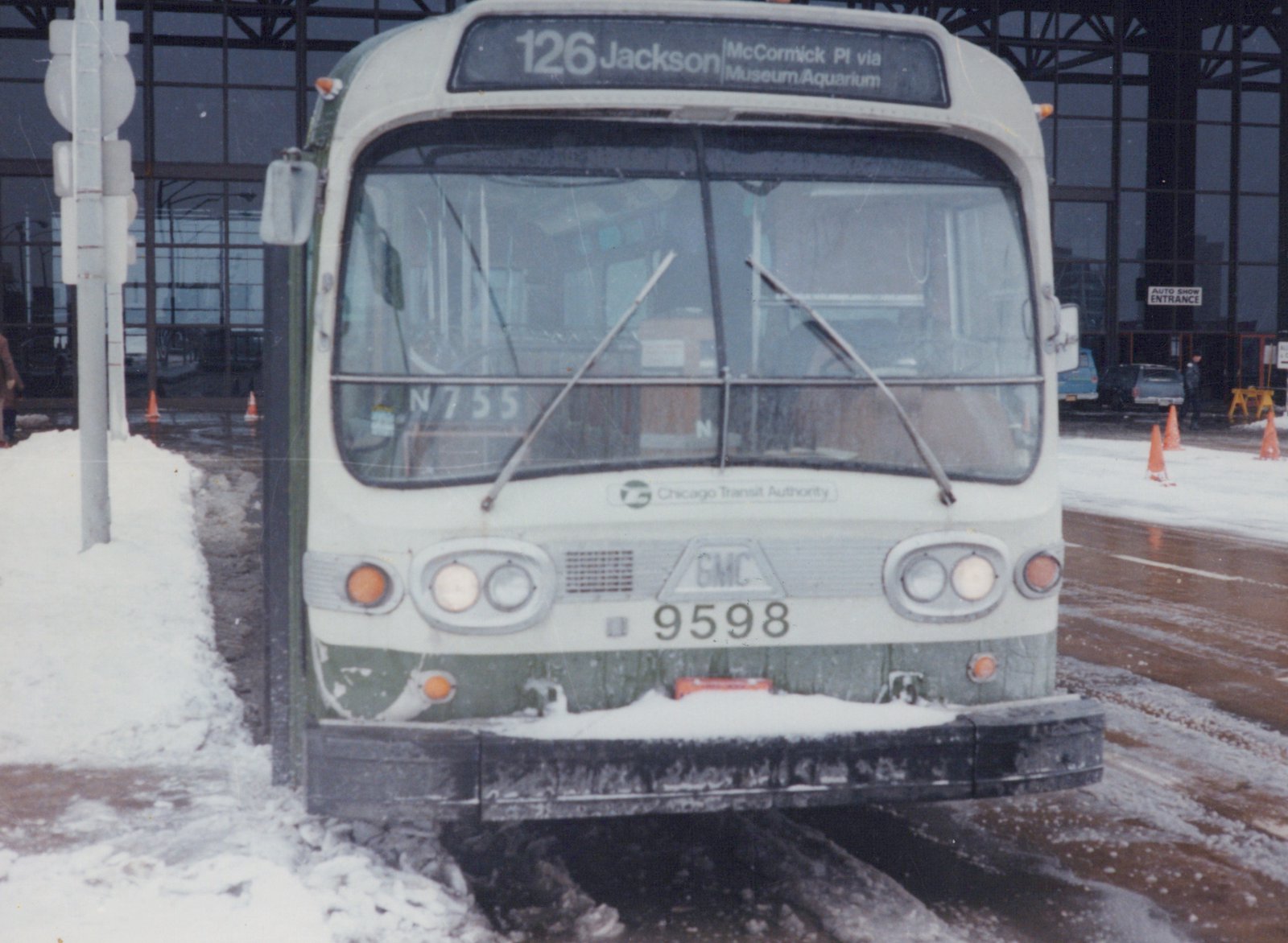 Front view of a white and green CTA bus with the number 9598 and destination sign reading 126 Jackson McCormick PI via Museum Aquarium, parked on a snowy street in front of a large building with a sign for the Auto Show Entrance.