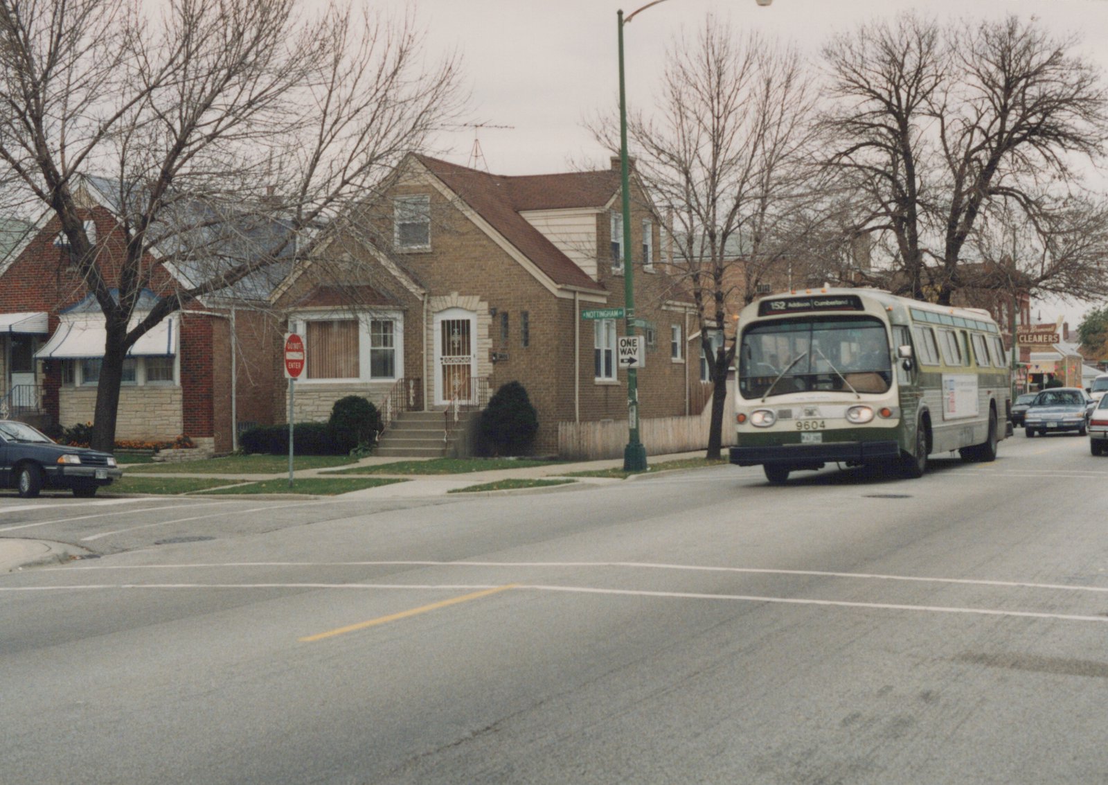 A white and green CTA bus numbered 9604 drives down a tree-lined residential street under an overcast sky, with street signs for Nottingham Avenue and a 'One Way' sign visible.