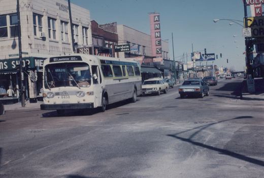 A white and green Chicago Transit Authority bus, number 9458, is on a city street with 1970s cars and storefronts including a sign for Florsheim shoes and a tall Anne's sign.