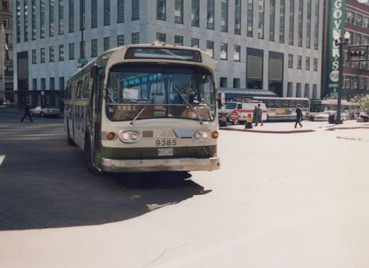 A front three-quarter view of a green and cream Chicago Transit Authority bus numbered 9385 on a sunny city street, with pedestrians and other vehicles in the background.