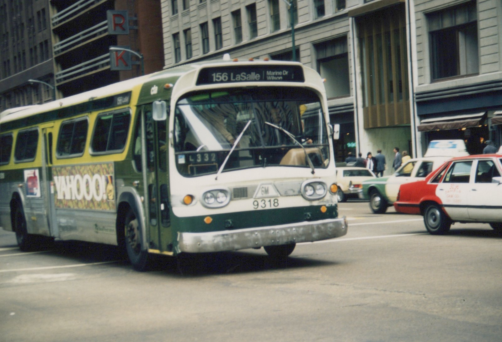 A green and cream Chicago Transit Authority bus, route 156 to LaSalle, drives down a city street with other cars, including taxis, and pedestrians nearby.