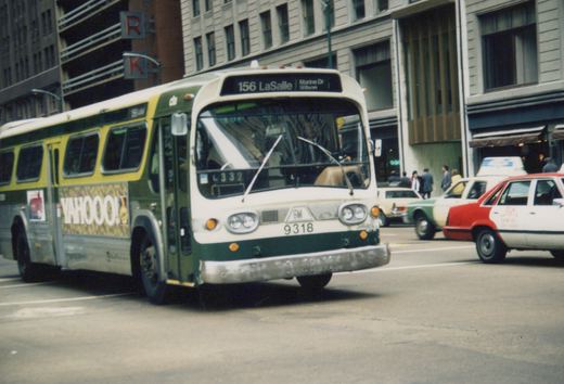 A green and cream Chicago Transit Authority bus, route 156 to LaSalle, drives down a city street with other cars, including taxis, and pedestrians nearby.