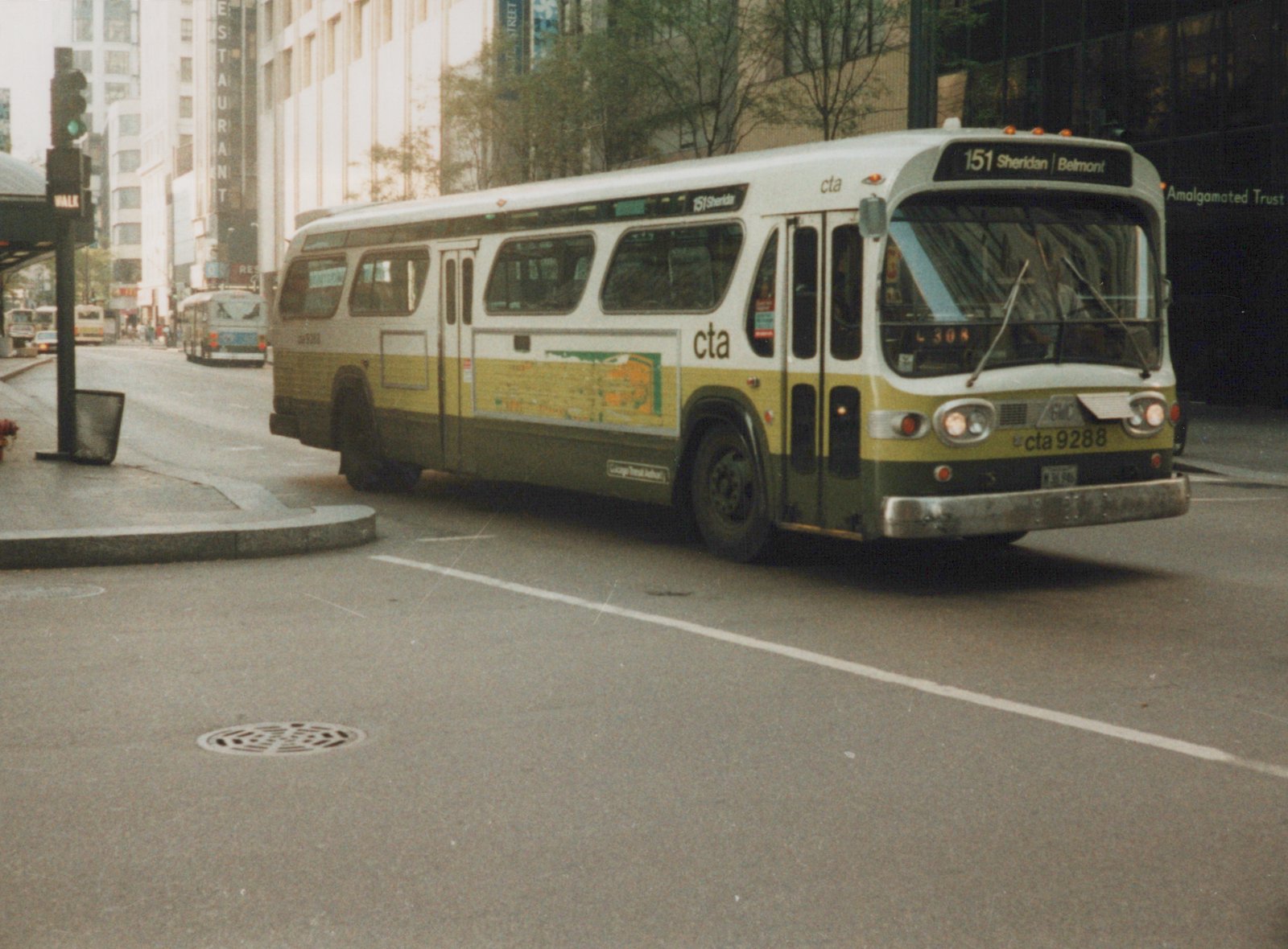 A white and green Chicago Transit Authority bus, number 9288, is driving on a city street with tall buildings in the background.