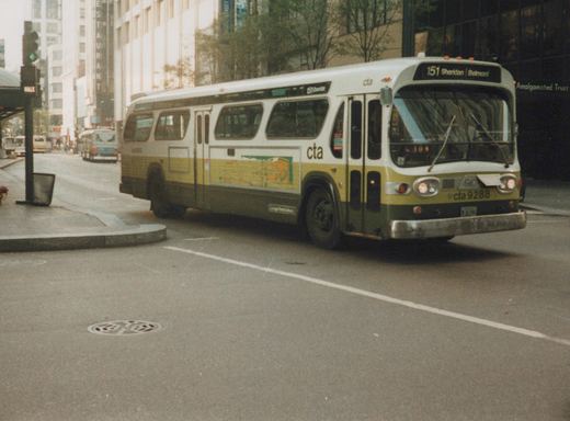A white and green Chicago Transit Authority bus, number 9288, is driving on a city street with tall buildings in the background.