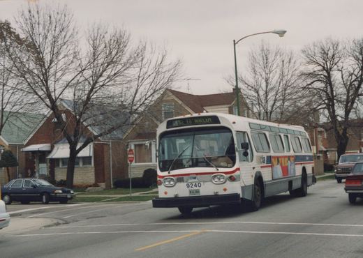 A white CTA bus with a red stripe, number 9240, is driving down a street lined with bare trees and houses; the destination sign reads '152 to HARLEM'.