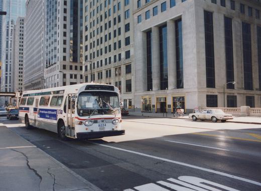 A white and blue CTA bus, marked with the number 9224 and destination 'North Terminal,' is driving on a city street lined with tall buildings.