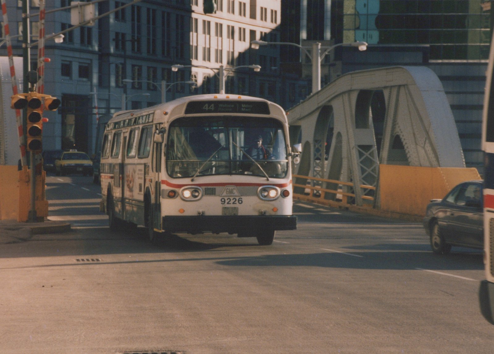 A white and red CTA bus, number 9226, turns on a city street near a steel bridge, with a driver visible and other cars nearby.