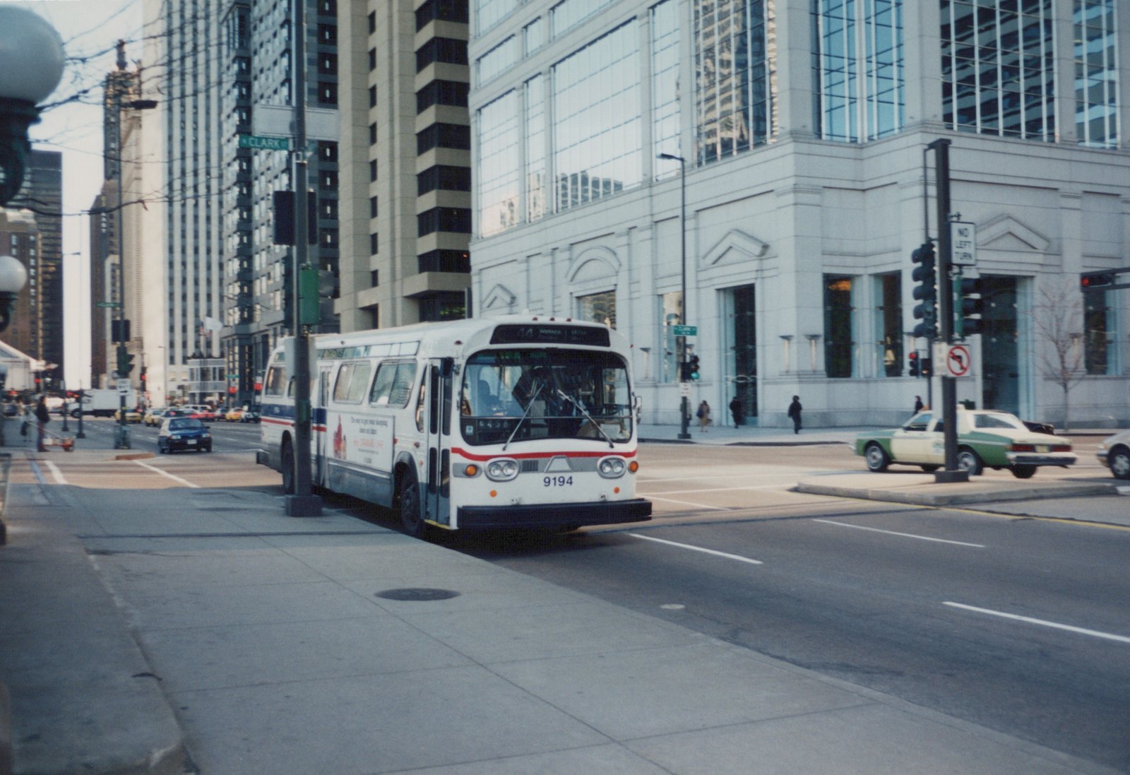 A white and red CTA bus with the number 9194 is stopped on a city street with tall buildings in the background and a green and white taxi nearby.