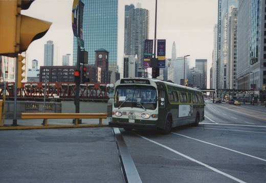A green and white CTA bus with the number 9789 and destination sign reading 'North Terminal' is stopped at an intersection in a city with tall buildings and elevated train tracks in the background.