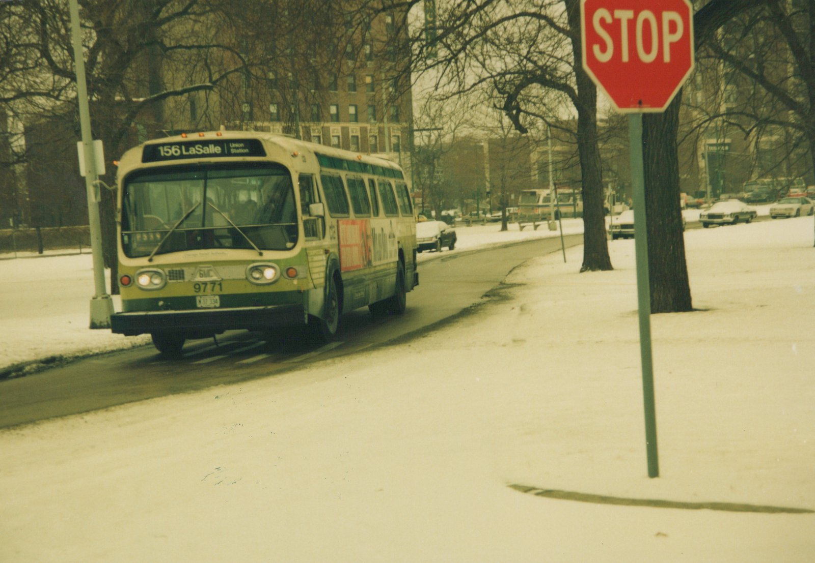 A vintage CTA bus, number 9771, drives down a snow-covered street in winter with a stop sign visible on the right and bare trees lining the road.