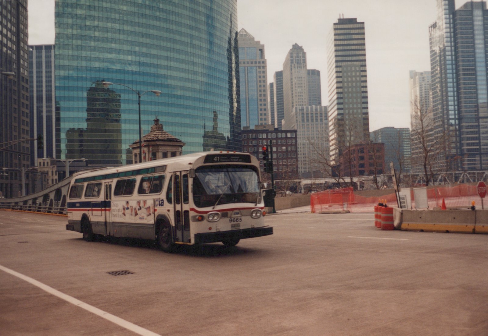 A white CTA bus with the number 9665 and route 41 is driving on a city street, with tall glass buildings and construction barriers in the background.