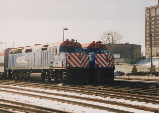 Two diesel locomotives with Metra livery, numbered 176 and 168, are parked on parallel tracks in a snowy yard.