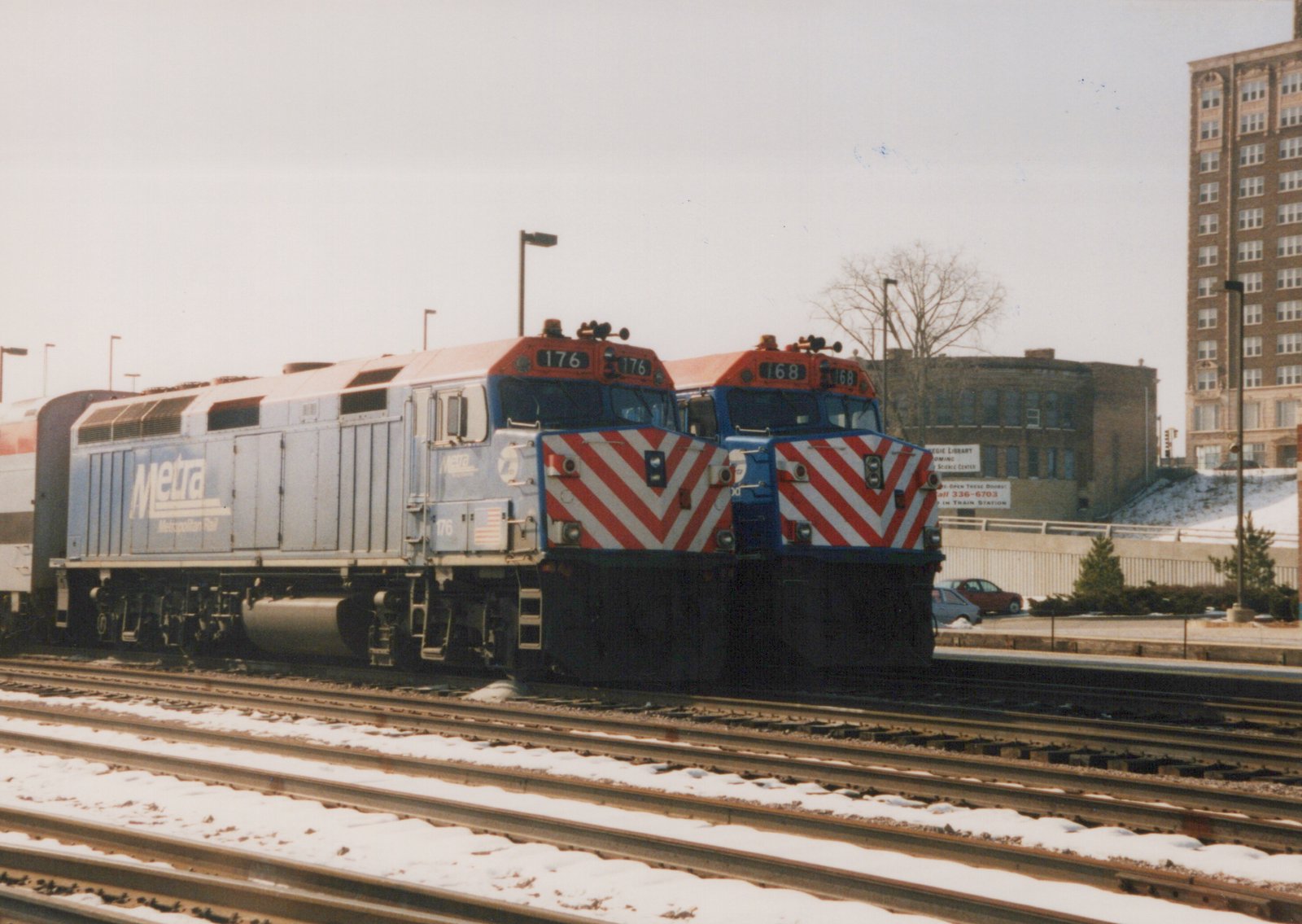 Two diesel locomotives with Metra livery, numbered 176 and 168, are parked on parallel tracks in a snowy yard.