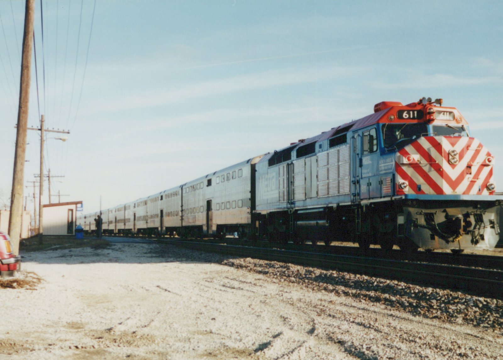 A blue and red Metra diesel locomotive with the number 611 on the front, pulling a long line of silver double-decker commuter cars on a gravel-lined track.