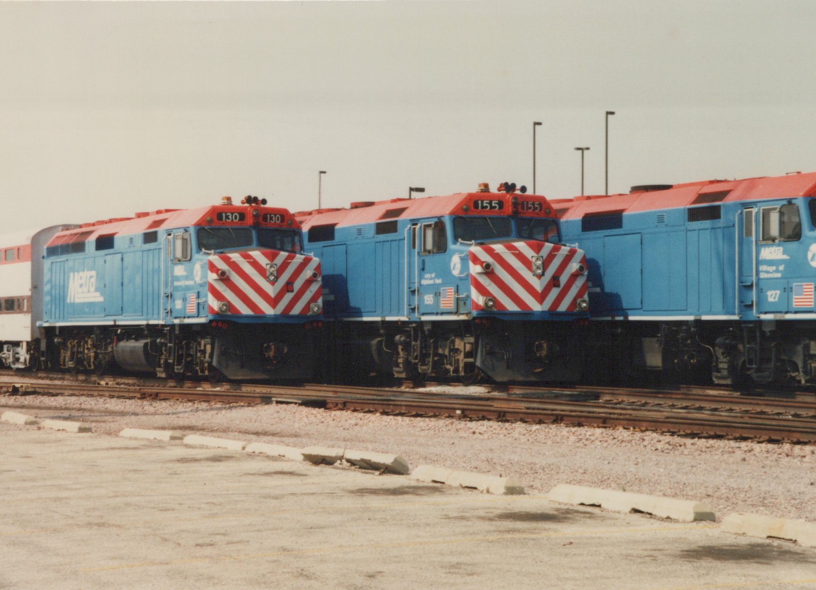 Three blue and red Metra locomotives with white chevrons on their noses are parked side by side on parallel tracks in a gravel yard under an overcast sky.