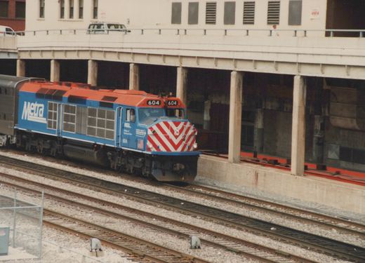 A blue and orange Metra locomotive, number 604, pulling a double-decker passenger car under an elevated highway in Chicago.