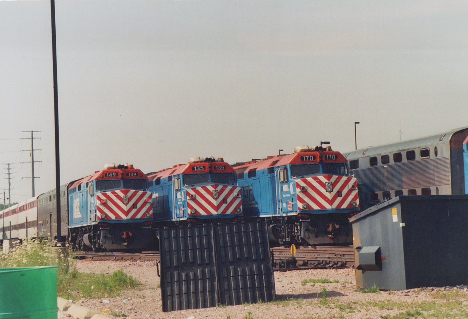 Three blue and red Metra diesel locomotives with numbers 149, 135, and 170 are parked side by side in a rail yard under an overcast sky.