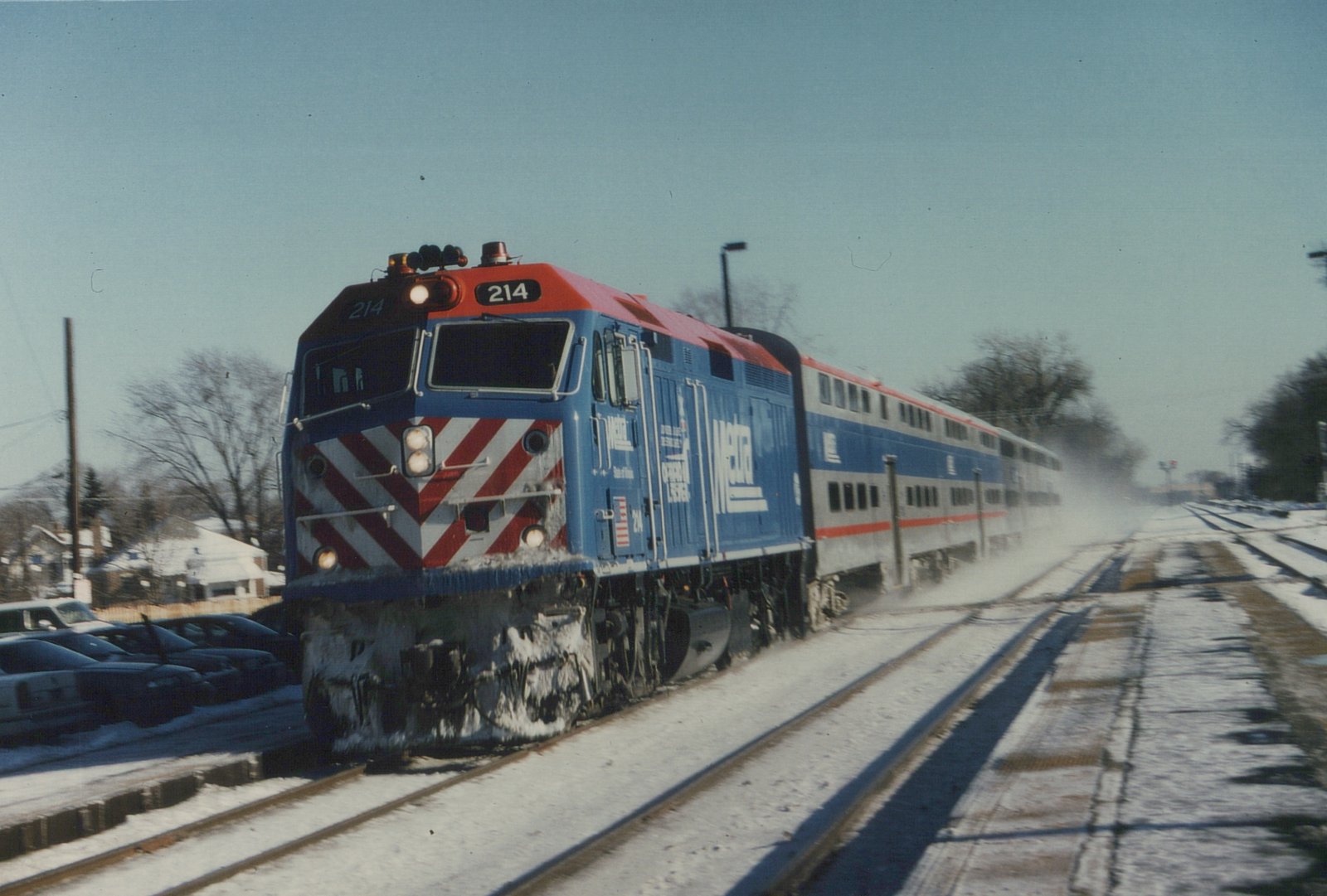 A blue and red Metra diesel locomotive pulling double-decker commuter cars on snow-covered tracks.