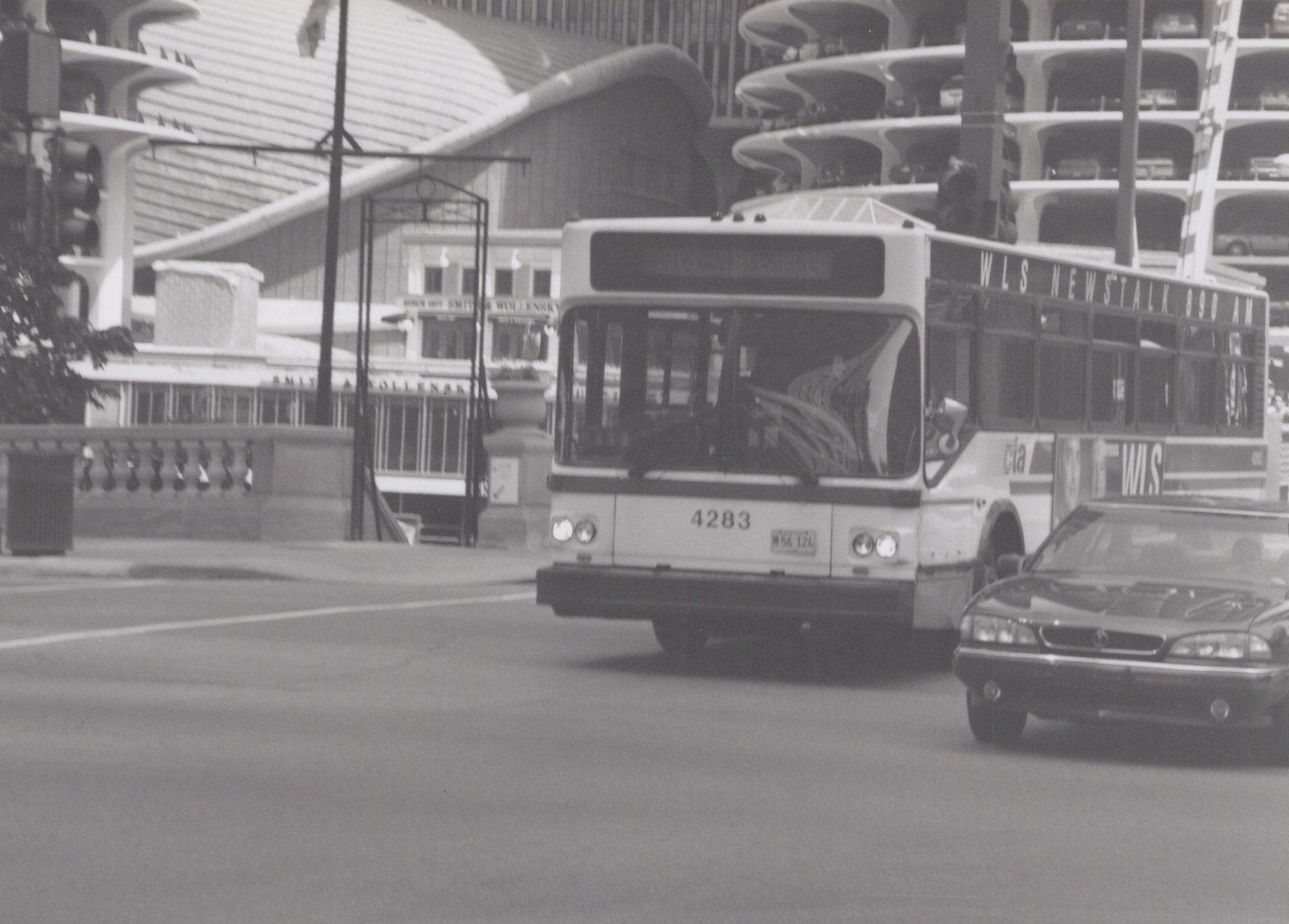 A black and white photograph shows a CTA bus numbered 4283 driving on a city street with a modern building and a restaurant sign in the background.