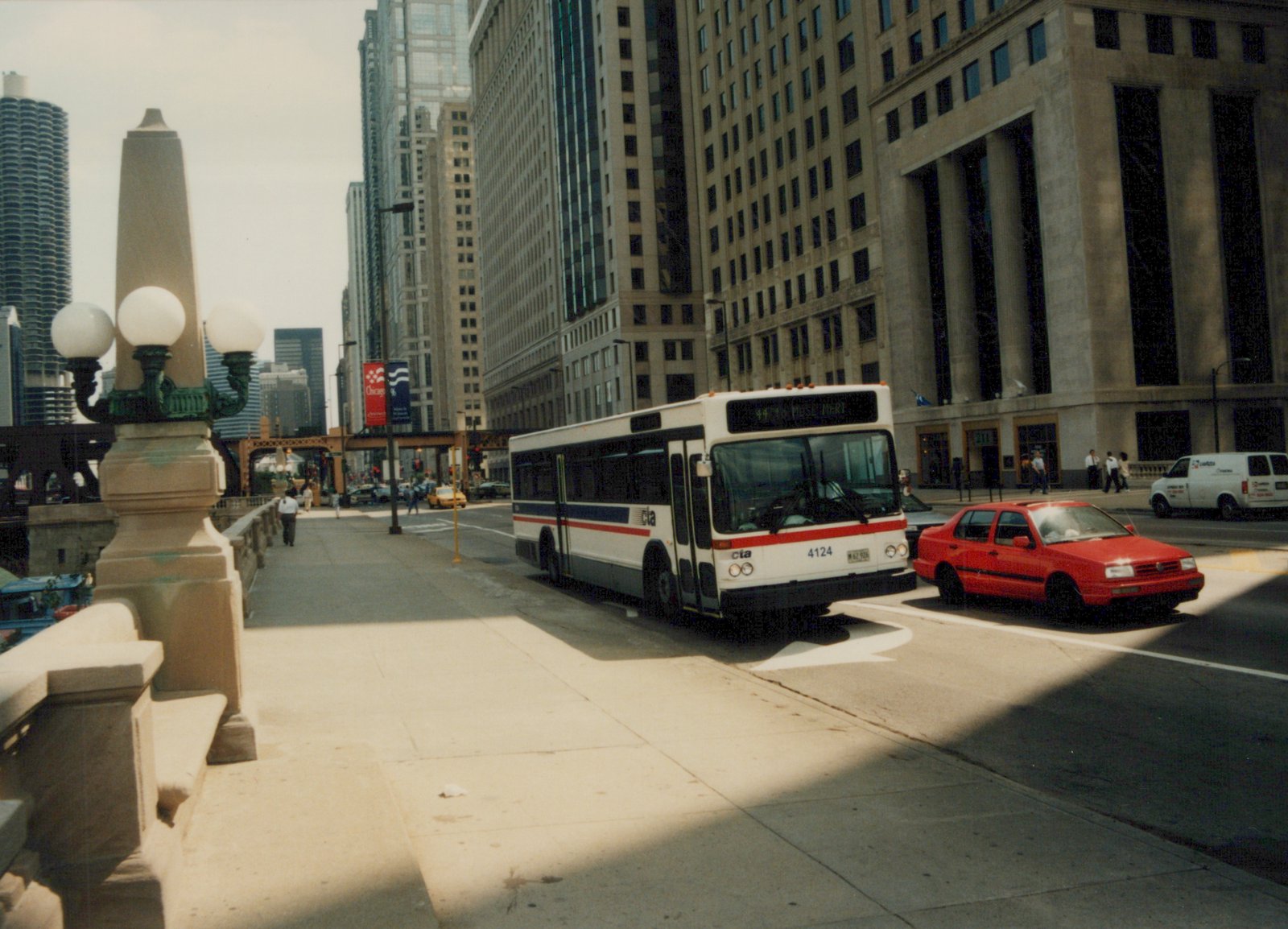 A white, blue, and red Chicago Transit Authority bus, number 4124, is on a city street with tall buildings and a red car nearby.