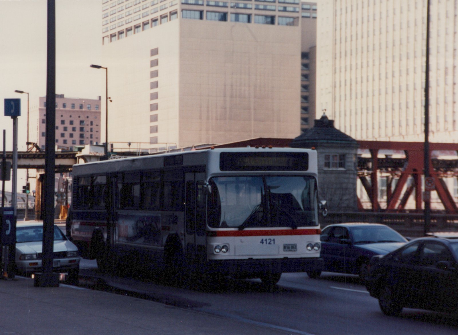 Front three-quarter view of a white and red Chicago Transit Authority bus, number 4121, on a city street with tall buildings and a bridge in the background.