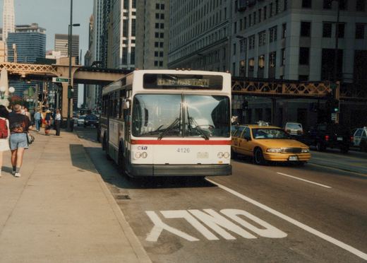 A white and red CTA bus numbered 4126 is stopped on a city street under an elevated train track, with pedestrians on the sidewalk and a yellow taxi nearby.
