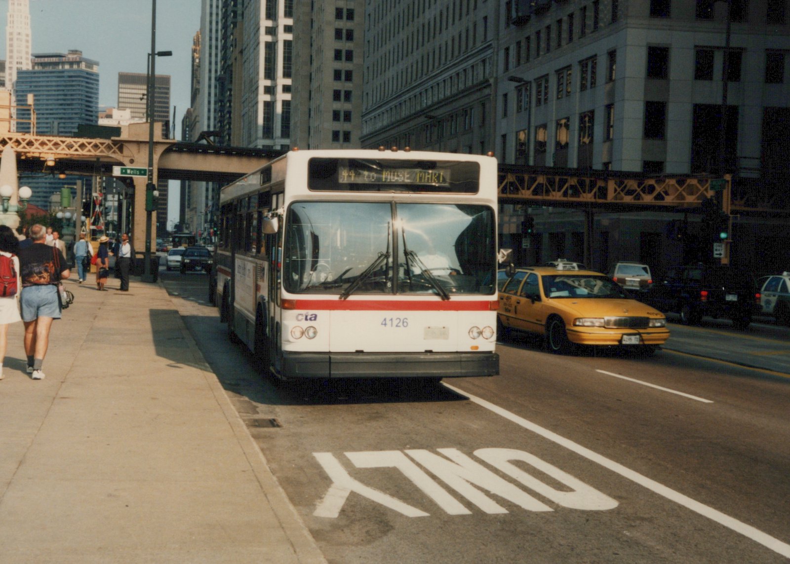 A white and red CTA bus numbered 4126 is stopped on a city street under an elevated train track, with pedestrians on the sidewalk and a yellow taxi nearby.