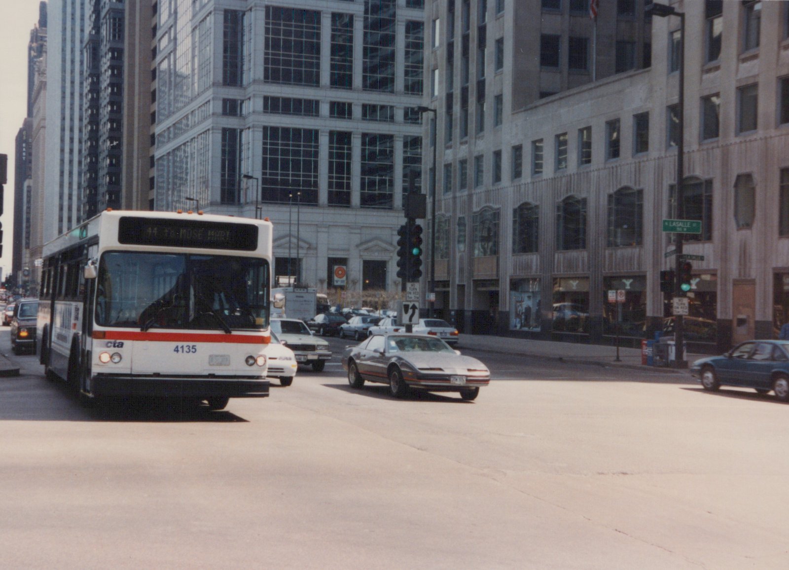 A white and red Chicago Transit Authority bus, number 4135, drives on a city street with other cars and tall buildings in the background.