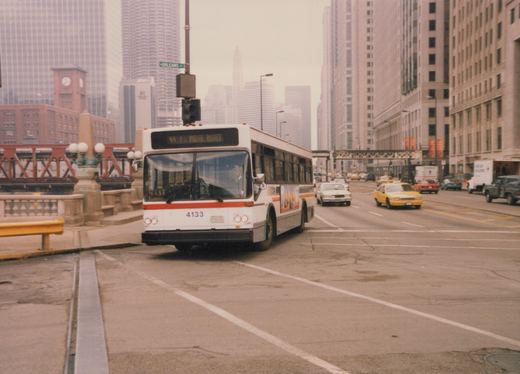 A white and red Chicago Transit Authority bus, number 4133, is stopped on a city street with tall buildings and other traffic in the background. A street sign for Orleans St is visible.