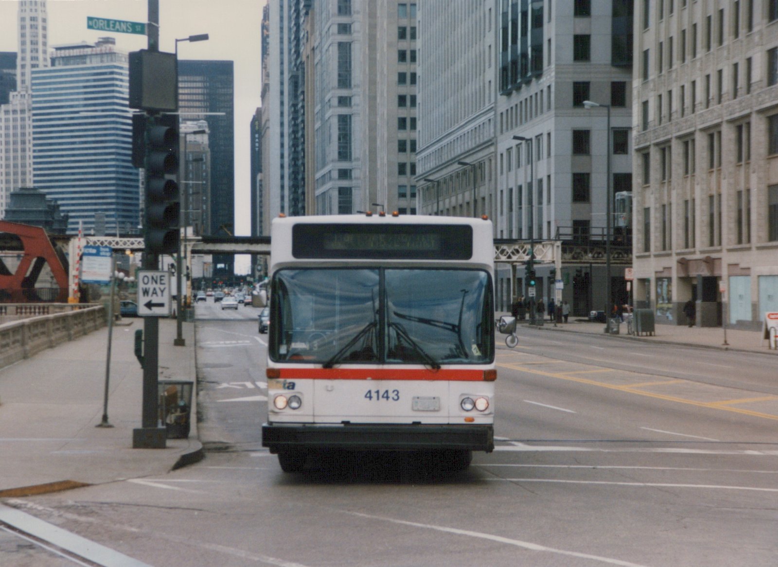 Front view of a white and red Chicago Transit Authority bus, number 4143, driving on a city street with tall buildings and a bridge in the background.