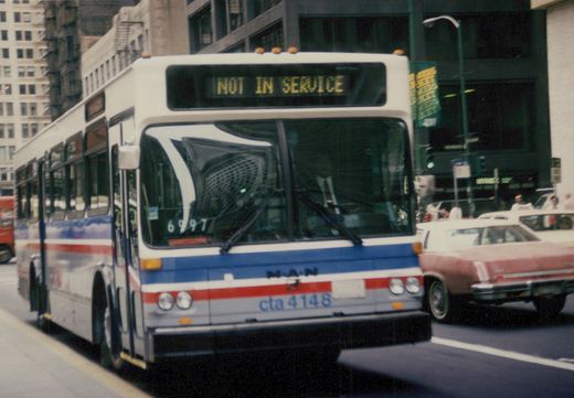 A white, blue, and red Chicago Transit Authority bus with the number 4148 on the front bumper and 'NOT IN SERVICE' on the destination sign, driving on a city street with a sedan alongside it.