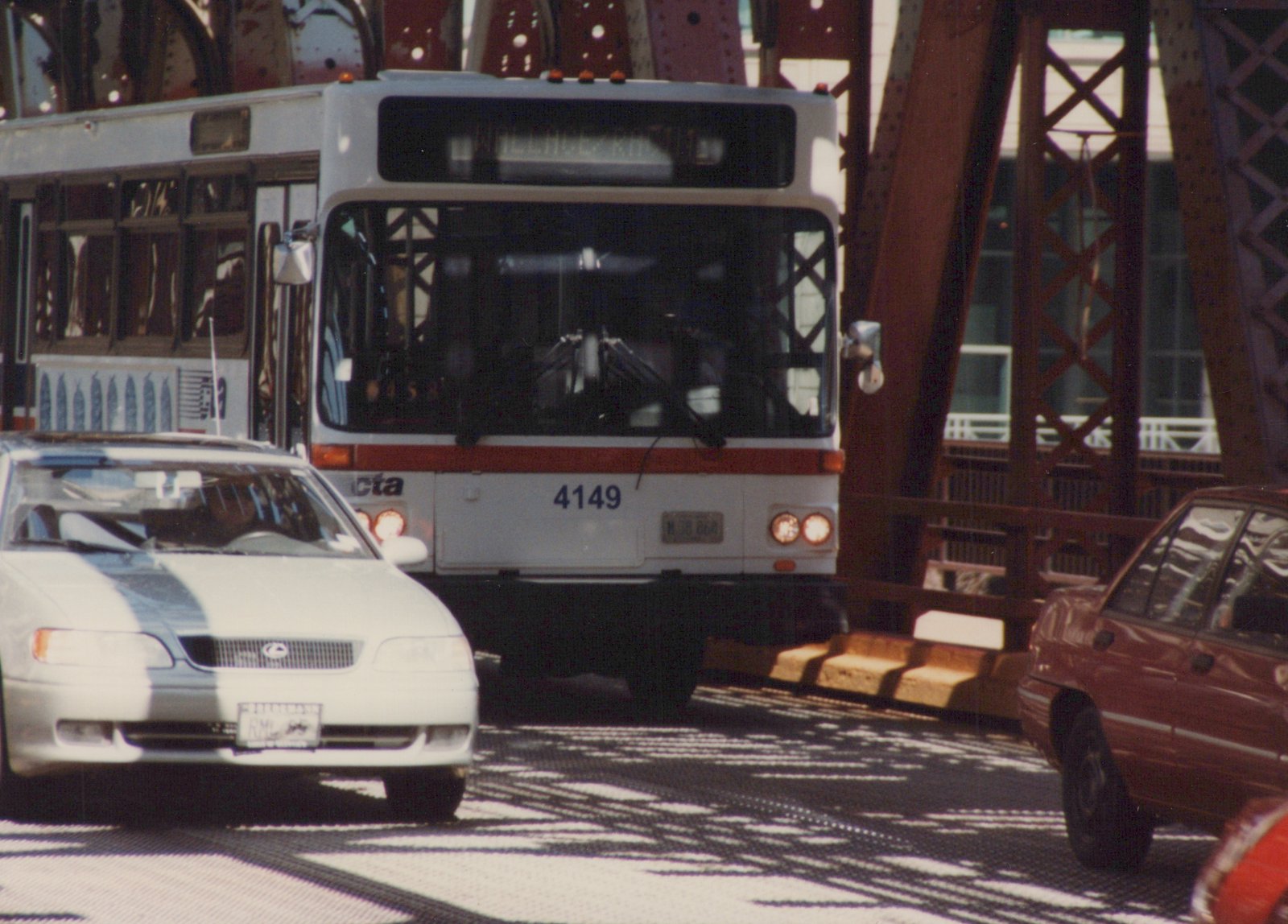 A white and red CTA bus with number 4149 is on a bridge, with a white car in front and a red car to the side, under a clear sky.