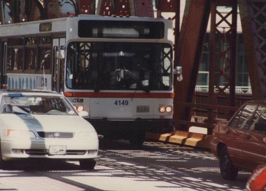 A white and red CTA bus with number 4149 is on a bridge, with a white car in front and a red car to the side, under a clear sky.