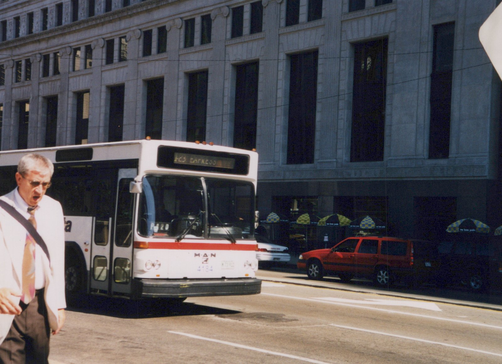 A white and red CTA bus, number 4184, is driving down a city street with a man walking on the sidewalk and a large stone building in the background.
