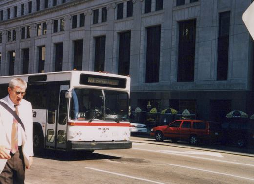 A white and red CTA bus, number 4184, is driving down a city street with a man walking on the sidewalk and a large stone building in the background.