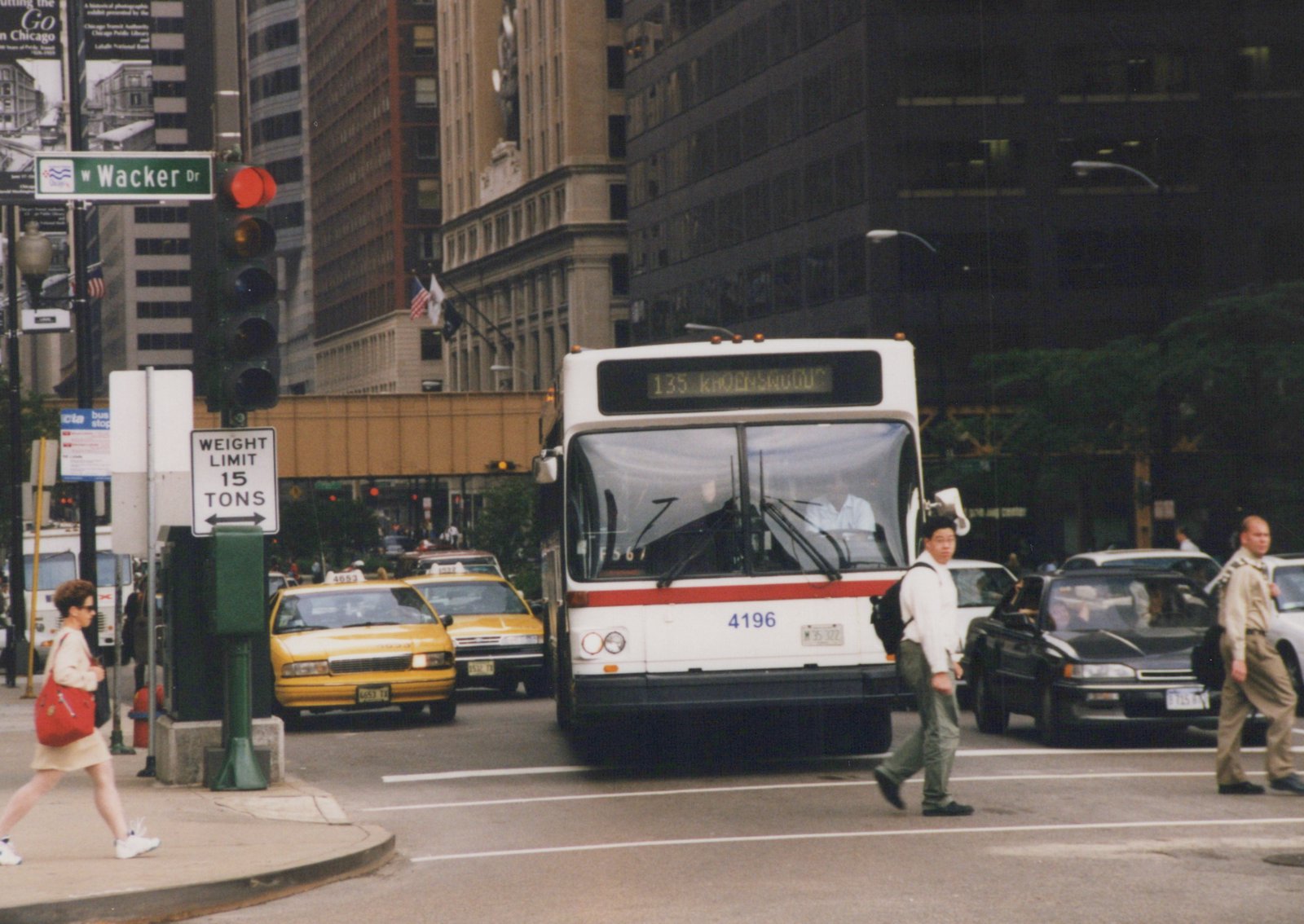 A white and red CTA bus numbered 4196 is stopped on a city street with pedestrians crossing in front and yellow taxis nearby, with a street sign for W Wacker Dr visible.