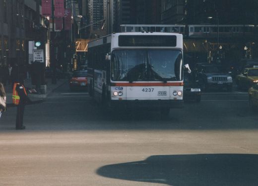 A white and red CTA bus with the number 4237 on the front is stopped on a city street with an elevated train in the background and other cars around it.