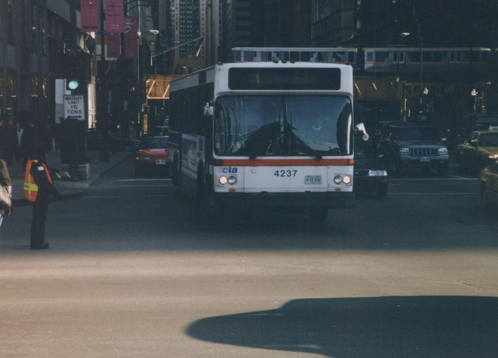 A white and red CTA bus with the number 4237 on the front is stopped on a city street with an elevated train in the background and other cars around it.