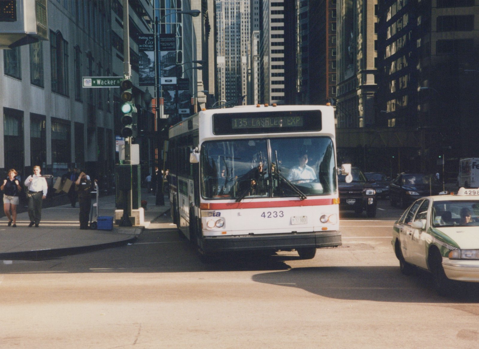 A white and red CTA bus with the number 4233 on the front is driving on a city street with tall buildings and pedestrians nearby.