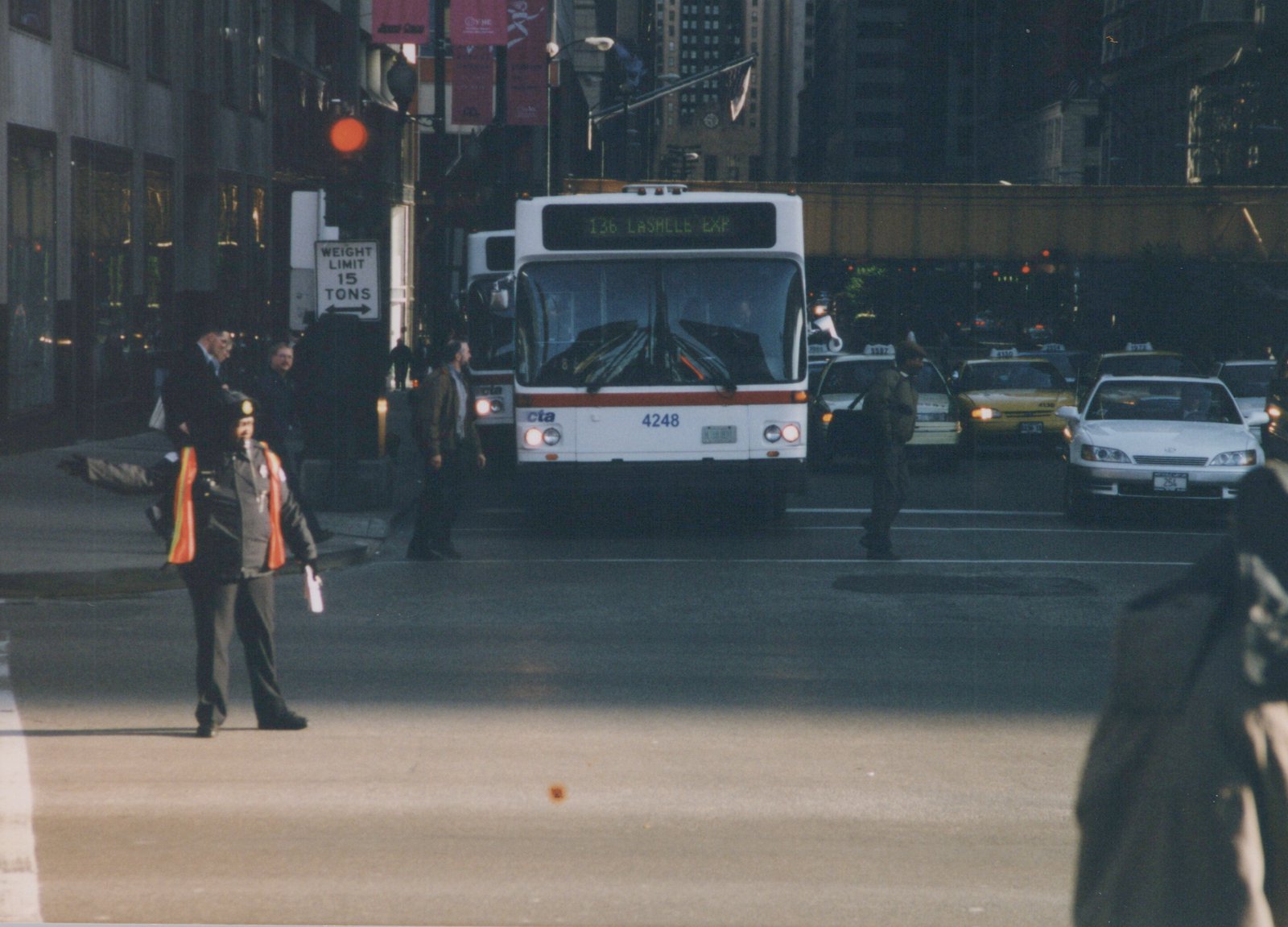 Front view of a white CTA bus numbered 4248 on route 136 Lasalle Express stopped at a busy city intersection with pedestrians and taxis, under an overpass at dusk.